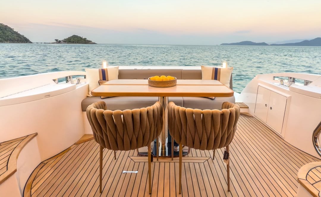 Aft-deck dining at dusk: a teak table with woven cushioned chairs and a bowl of lemons, set against a calm sea and distant islands.
