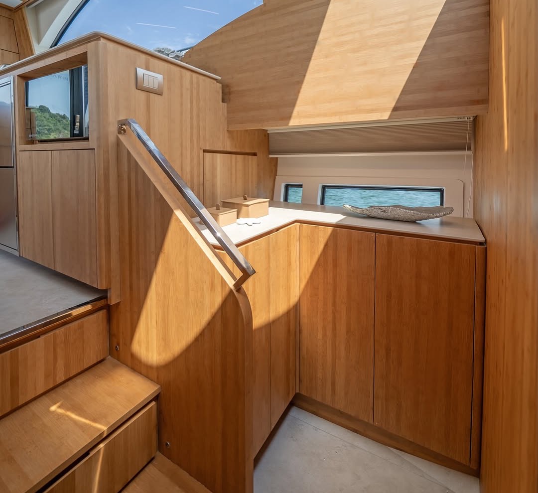 Bamboo joinery inside a yacht: a staircase, handrail and cabinetry crossed by a diagonal of natural sunlight.
