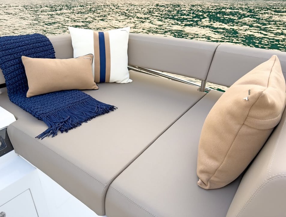 Detail of a yacht sunpad: a fringed navy knitted throw and sand-toned cushions, with sunlit water beyond.