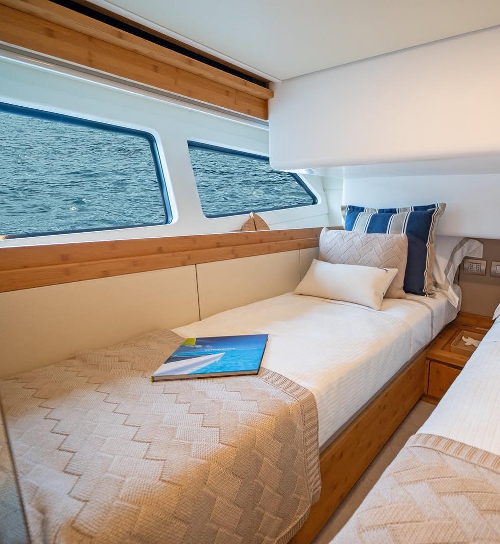 Twin guest cabin in a yacht interior: beds dressed in textured knit throws beneath long windows framing the sea.